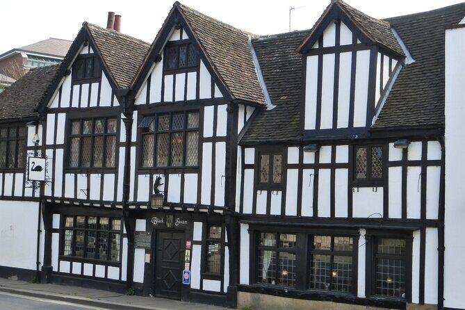 Black and white timber-framed building with diamond-paned windows and multiple steep gables, identified as the Black Swan with a hanging wooden sign featuring a black swan silhouette