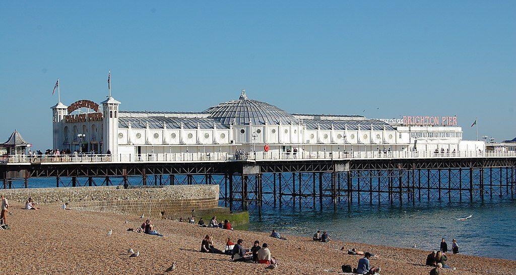 Brighton Palace Pier extending over the sea with people sitting on the pebble beach in the foreground under a clear blue sky