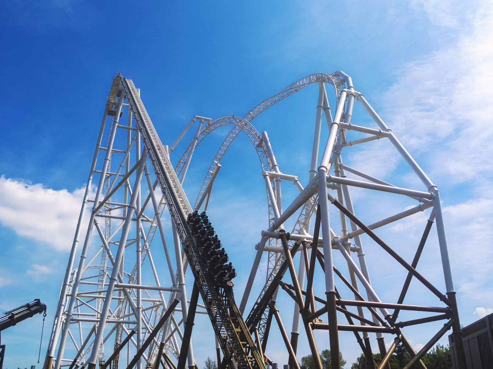 Roller coaster ascending a steep track with white and black metal supports against a blue sky with some clouds