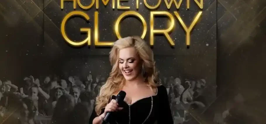 Blonde female singer in a black, beaded dress holding a microphone and smiling in front of a cheering crowd, with large gold "HOMETOWN GLORY" lettering above